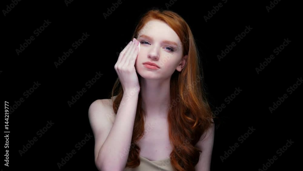 Beautiful young red haired woman cleaning her face with cotton pad isolated on black background Beautiful young red haired woman cleaning her face with cotton pad isolated on black background