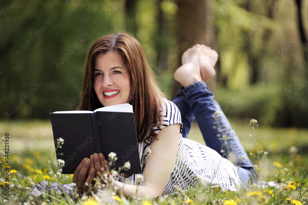Beautiful young brunette woman lying on the meadow with field flowers with a book in her hands. Romantic outdoor conception. Beautiful young brunette woman lying on the meadow with field flowers with a book in her hands. Romantic outdoor conception.