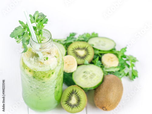 Cucumber smoothies in the bottle, kiwi, parsley, and banana on white wooden table.
