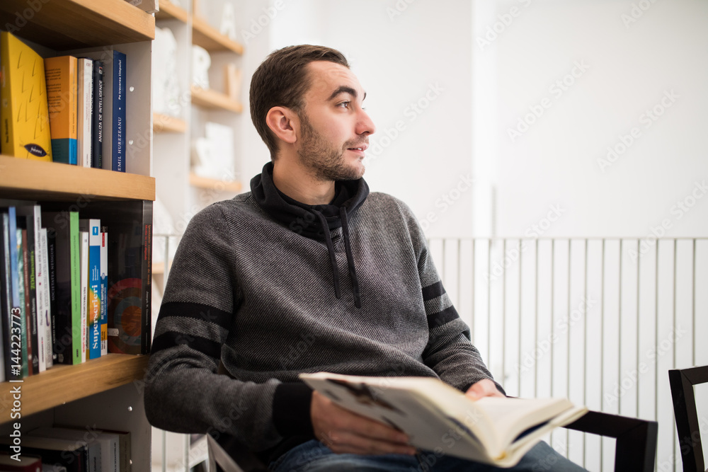 Handsome male student reading a book sitting on the floor in a bookshop