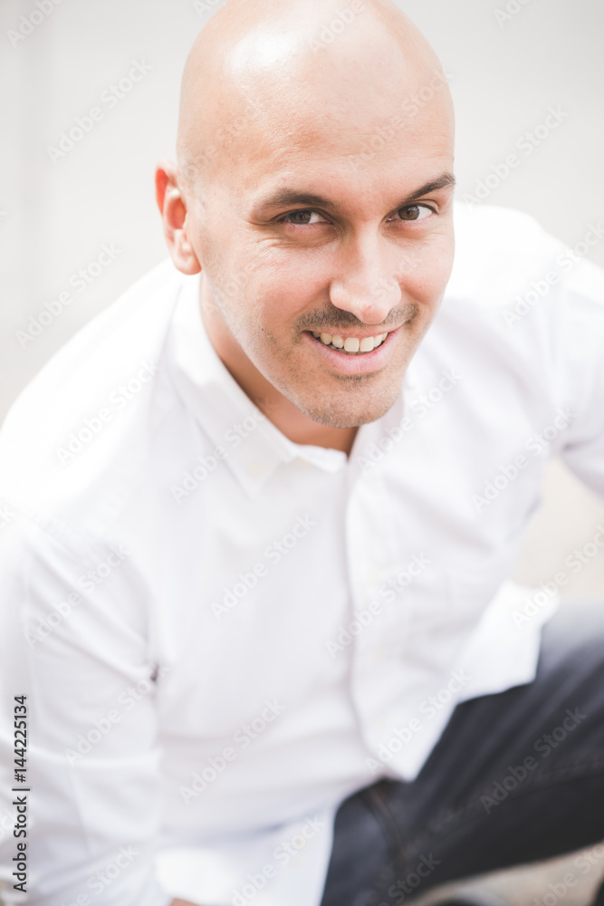 Fototapeta premium Young man caucasian sitting outdoor in the city looking away, smiling - customer, city living, positive feelings concept