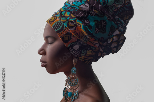 Young beautiful African woman in traditional style with scarf, earrings crying, isolated on gray background. racism, depression or loneliness concept.. photo