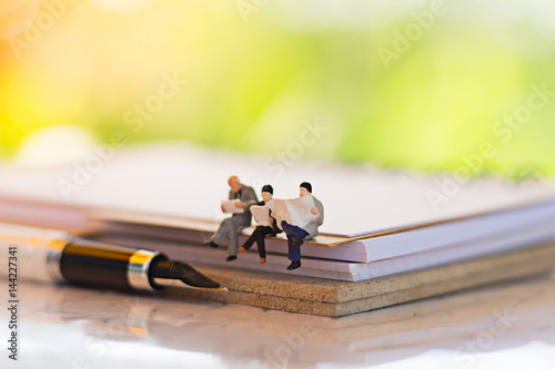 Miniature people sitting on book using as background education or business concept