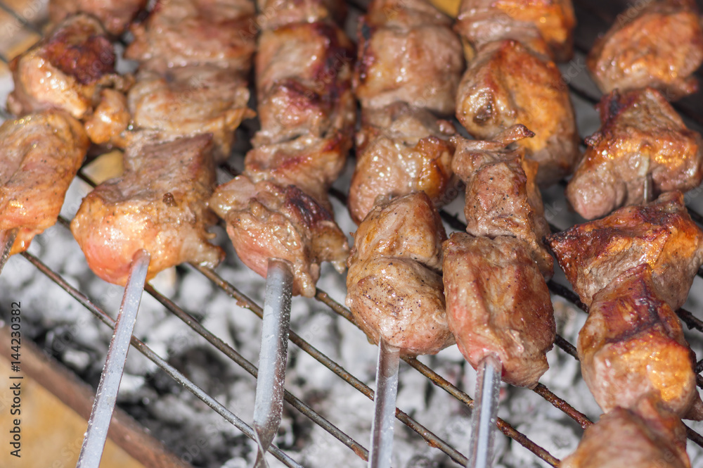 Pieces of tasty pork on skewers cooking outdoor on smoldering carbons
