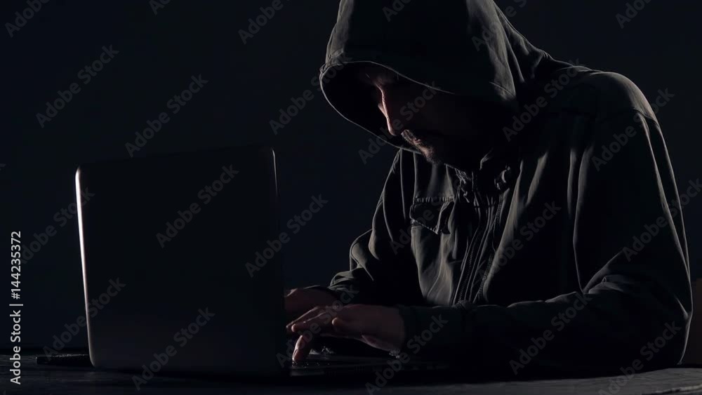 Cyber crime and computer virus concept with hooded faceless person working on laptop