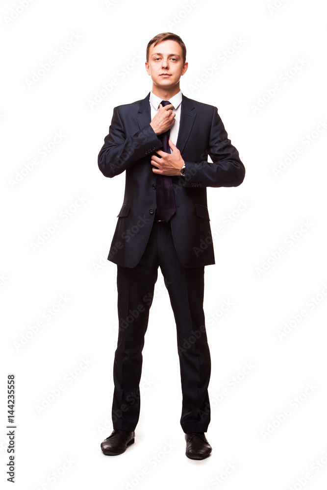 Stylish young man in suit and tie. Business style. Handsome man is standing, looking at the camera and fixing his tie Stylish young man in suit and tie. Business style. Handsome man is standing, looking at the camera and fixing his tie