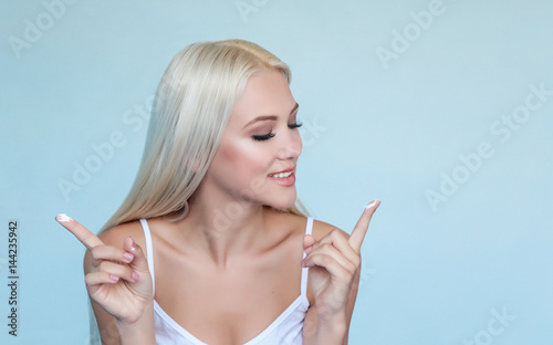 Luxury beautiful blonde girl or woman with clear skin and blue eyes show white cream on fingers. Сosmetology procedure with cream. Smiling girl in white shirt with cream on hands. Smear cream 