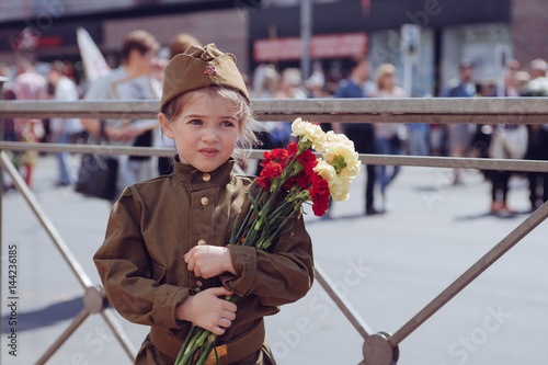 Portrait of a little girl in military uniform with flowers on holiday May 9, Russia