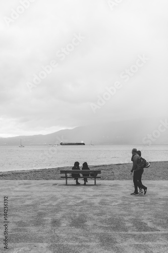 Two people sit on a bench looking out towards English Bay, Vancouver BC.