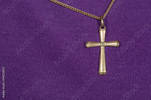 ein christliches Kreuz wird an einer goldenen Kette auf einem Kleidungsstück getragen