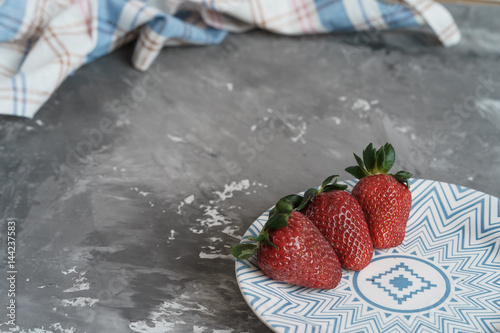 three strawberries on a palte on a concrete background, close up photo