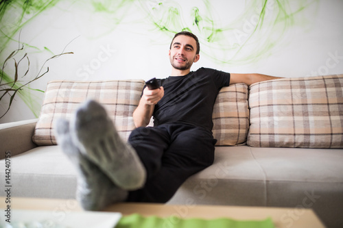 Man sitting on a sofa watching tv holding remote control at home photo