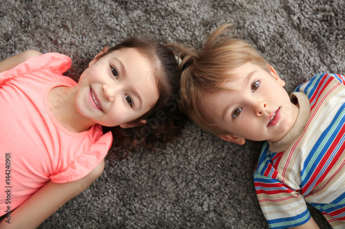 Cute little children lying on carpet at home