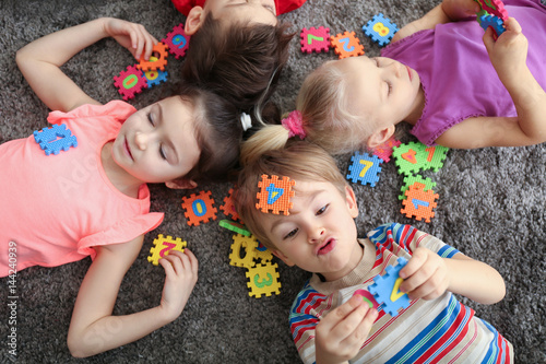 Cute little children playing with colorful figures while lying on carpet at home