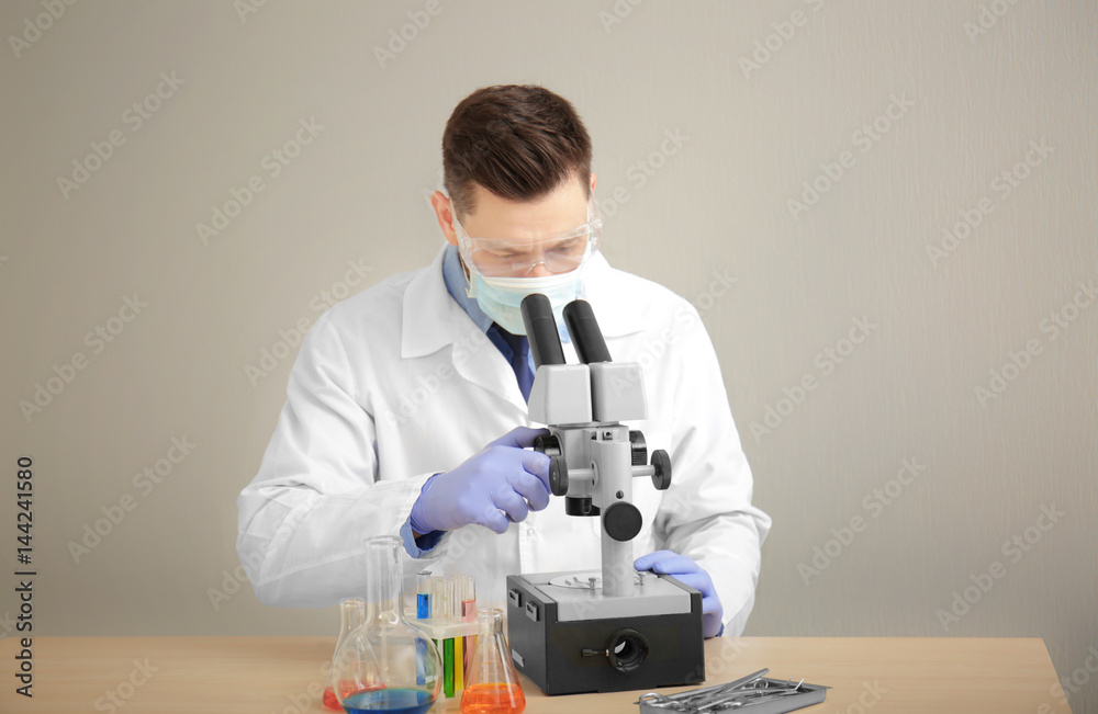 Young doctor working with microscope at table on light background Young doctor working with microscope at table on light background