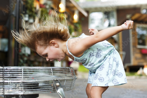 Side view of girl screaming while enjoying breeze from electric fan