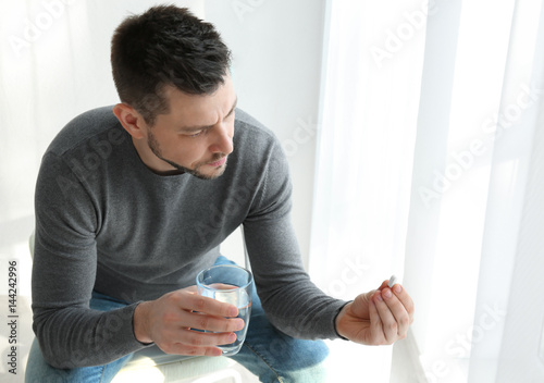 Handsome young man taking pill at home