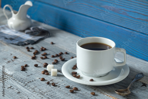 Coffee cup, beens and a jug on a background of blue boards