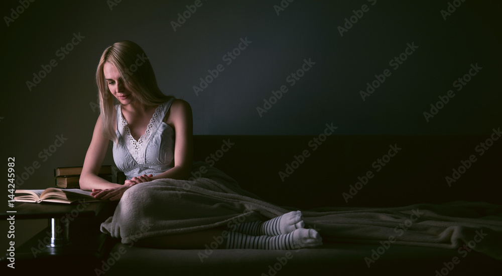 Fototapeta premium Girl enthusiastically reading a book best-selling house under a rug on a comfortable sofa with a lamp