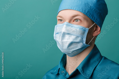 male surgeon in mask on blue background, close up