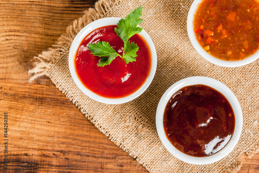 Three kinds of red tomato sauce on a wooden cutting board: traditional classic ketchup, barbecue sauce, sweet and sour Chinese sauce. Top view copy space Three kinds of red tomato sauce on a wooden cutting board: traditional classic ketchup, barbecue sauce, sweet and sour Chinese sauce. Top view copy space