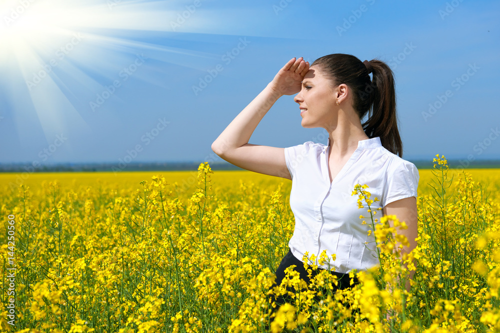 Business woman looking into the distance. Young girl in yellow flower field. Beautiful spring landscape, bright sunny day, rapeseed Business woman looking into the distance. Young girl in yellow flower field. Beautiful spring landscape, bright sunny day, rapeseed
