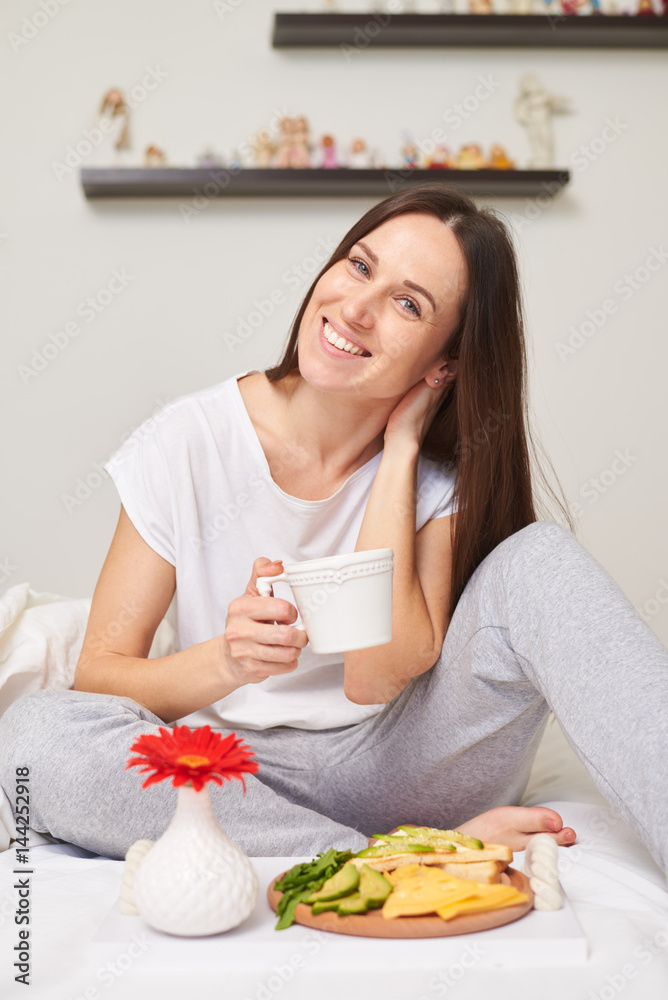 Smiling woman in pajamas eats organic breakfast