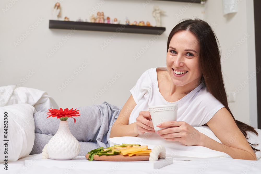 Charming girl lying in bed has her romantic breakfast