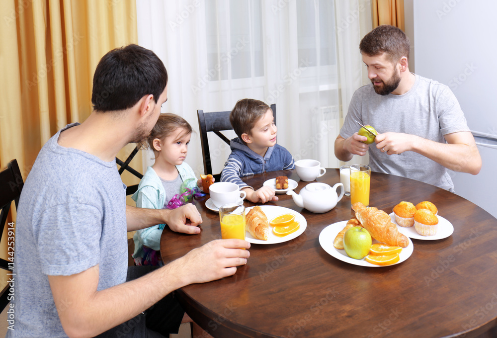 Male gay couple with children having breakfast in kitchen