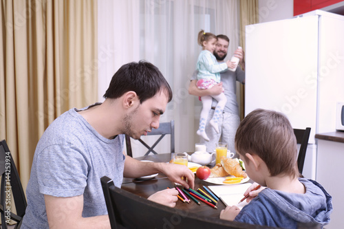 Male gay couple with children having breakfast in kitchen