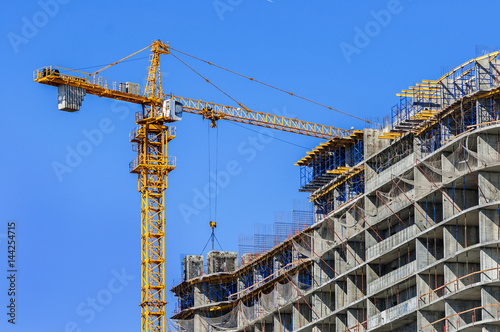 Construction site. Construction crane and high-rise building under construction against blue sky.