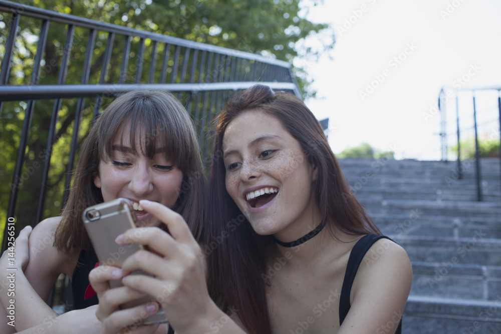 Smiling friends using cell phone on staircase Smiling friends using cell phone on staircase