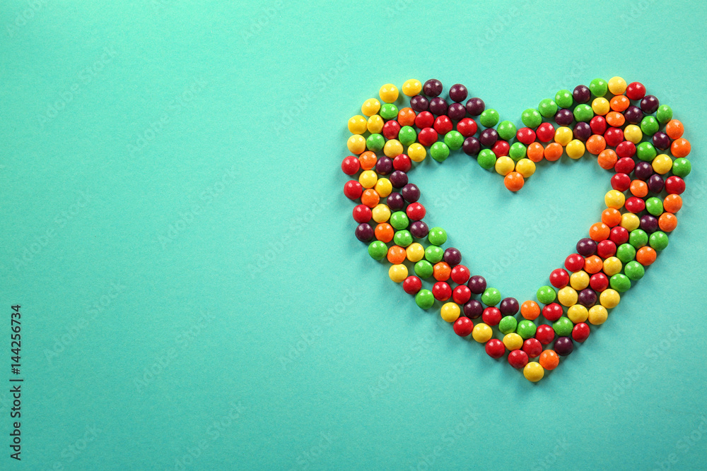 Colorful candies in shape of heart on color background