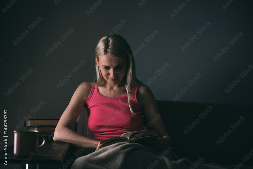 Girl enthusiastically reading a book best-selling house under a rug on a comfortable sofa with a lamp Girl enthusiastically reading a book best-selling house under a rug on a comfortable sofa with a lamp