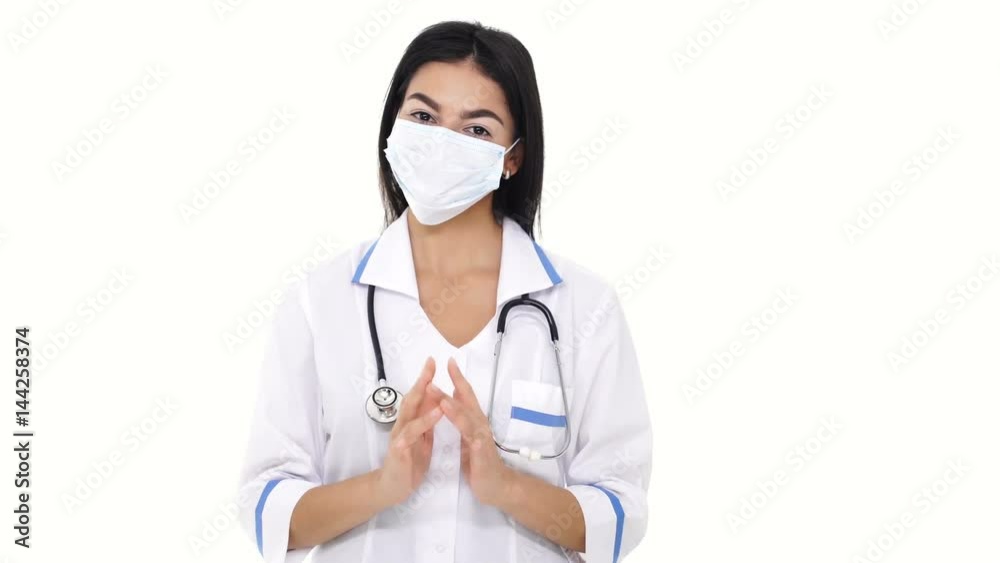 Wily young female nurse wearing white lab face mask fingering over and smiling isolated Wily young female nurse wearing white lab face mask fingering over and smiling isolated