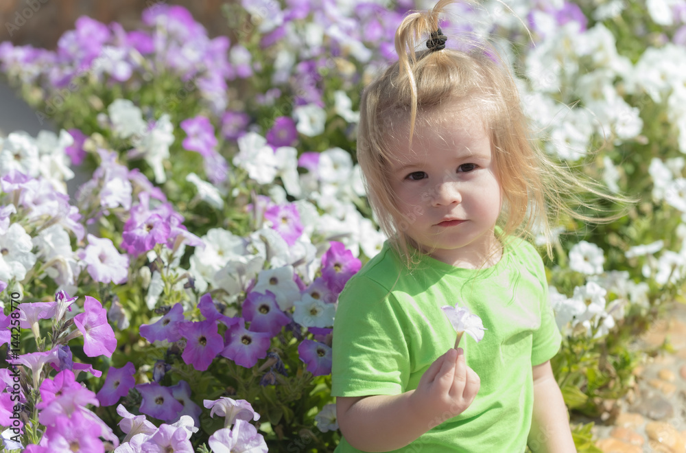 Cute baby boy playing at flowerbed with blossoming flowers Cute baby boy playing at flowerbed with blossoming flowers