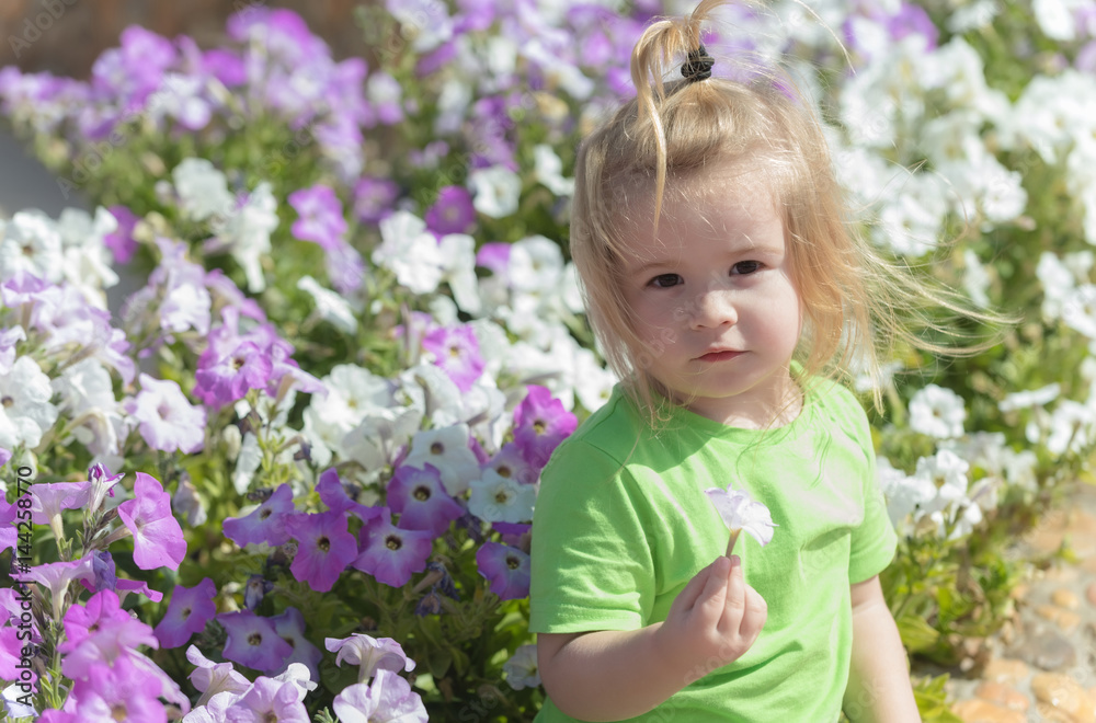 Cute baby boy playing at flowerbed with blossoming flowers