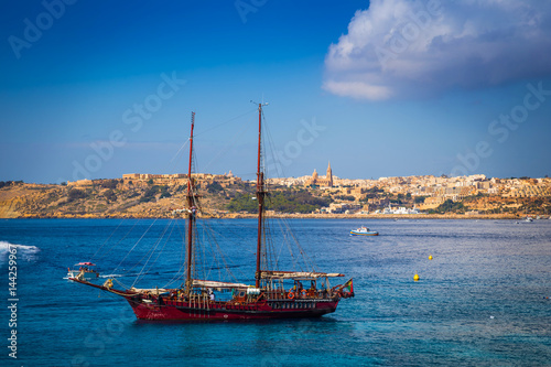 Blue Lagoon, Malta - Old sailing boat at the Island of Comino next to the famous Blue Lagoon with the Island of Gozo and town of Mgarr at the background on a sunny summer day