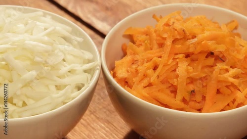 Chopped carrot and cabbage in white cup on wooden background close up. Ingredients for vegetable salad
