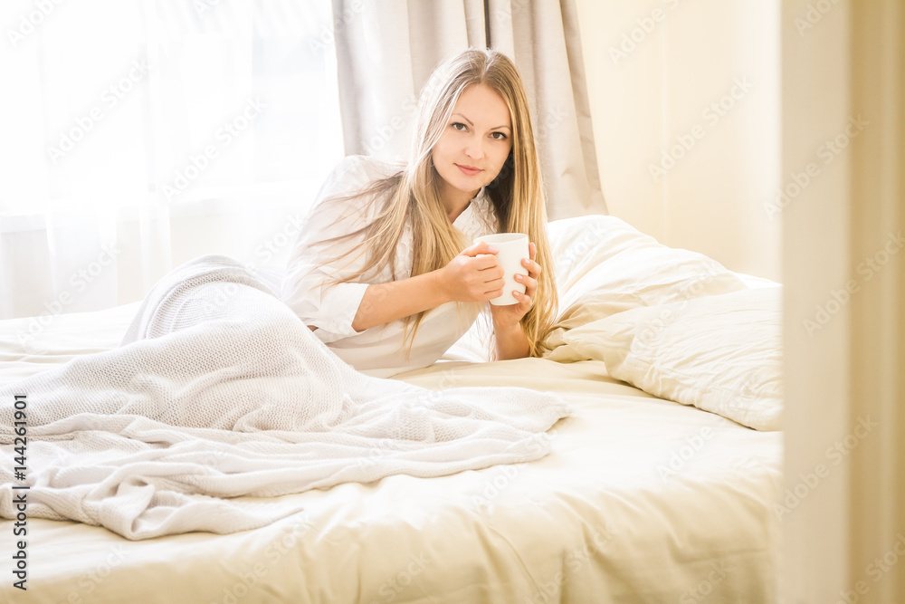 indoor portrait of young pretty happy woman with a cup of tea or coffee in bed, morning at home indoor portrait of young pretty happy woman with a cup of tea or coffee in bed, morning at home
