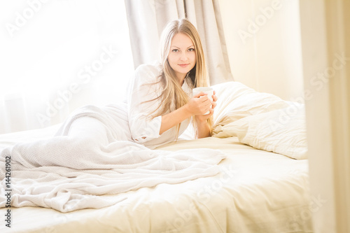 indoor portrait of young pretty happy woman with a cup of tea or coffee in bed, morning at home