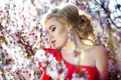 Happy young blonde woman in spring flowers garden lifestyle portrait.
