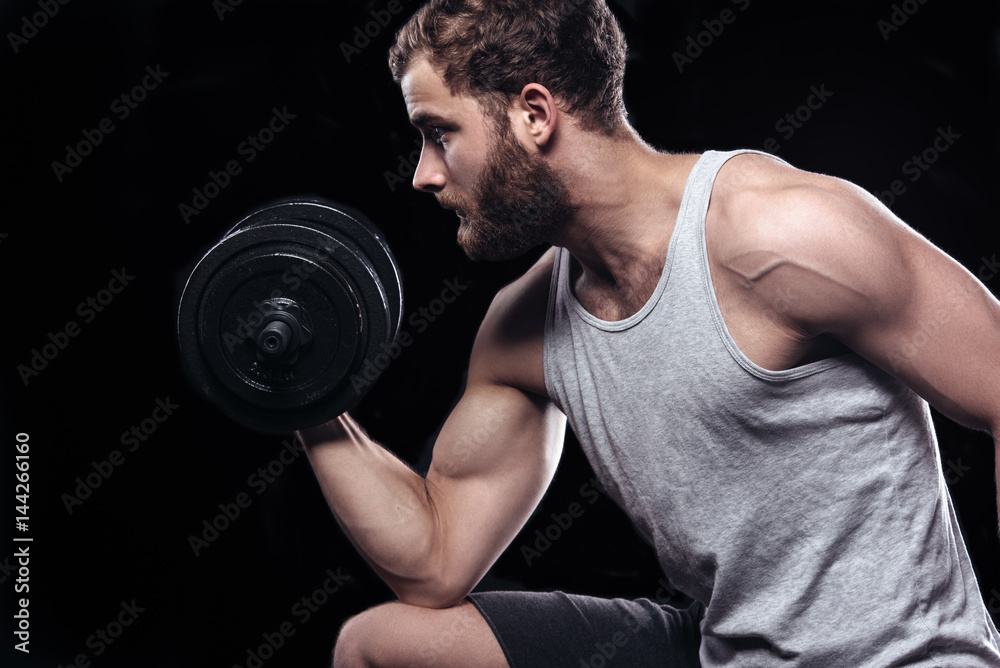 Handsome power athletic man with dumbbell confidently looking forward. Strong bodybuilder with six pack, perfect abs, shoulders, biceps, triceps and chest isolated on black background with copyspace