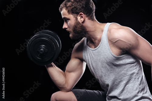 Handsome power athletic man with dumbbell confidently looking forward. Strong bodybuilder with six pack  perfect abs  shoulders  biceps  triceps and chest isolated on black background with copyspace