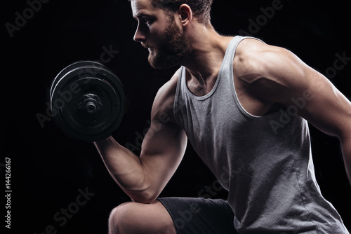 Handsome power athletic man with dumbbell confidently looking forward. Strong bodybuilder with six pack, perfect abs, shoulders, biceps, triceps and chest isolated on black background with copyspace © britanskiy