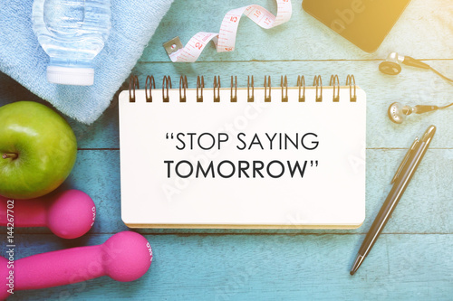 Fitness motivation quotes written on open notebook. Fitness equipment on wooden background.