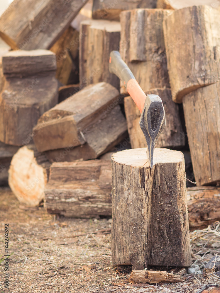 A hatchet with an orange handle and a large pile of wooden block of wood. A hatchet with an orange handle and a large pile of wooden block of wood.