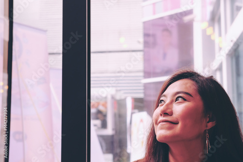 Portrait image of a beautiful Asian woman staying in restaurant and looking outside window with smiley face