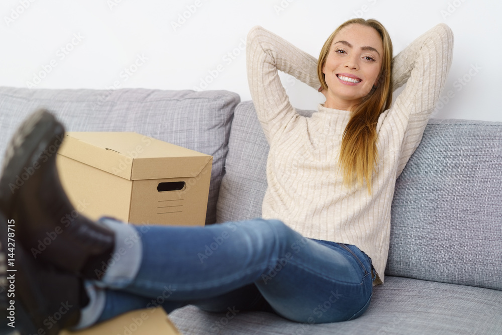 frau sitzt auf dem sofa mit mehreren kartons und legt entspannt die füße hoch
