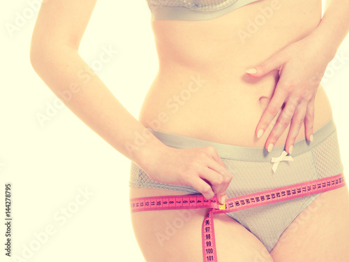 Woman in lingerie measuring her hips with measure tape.